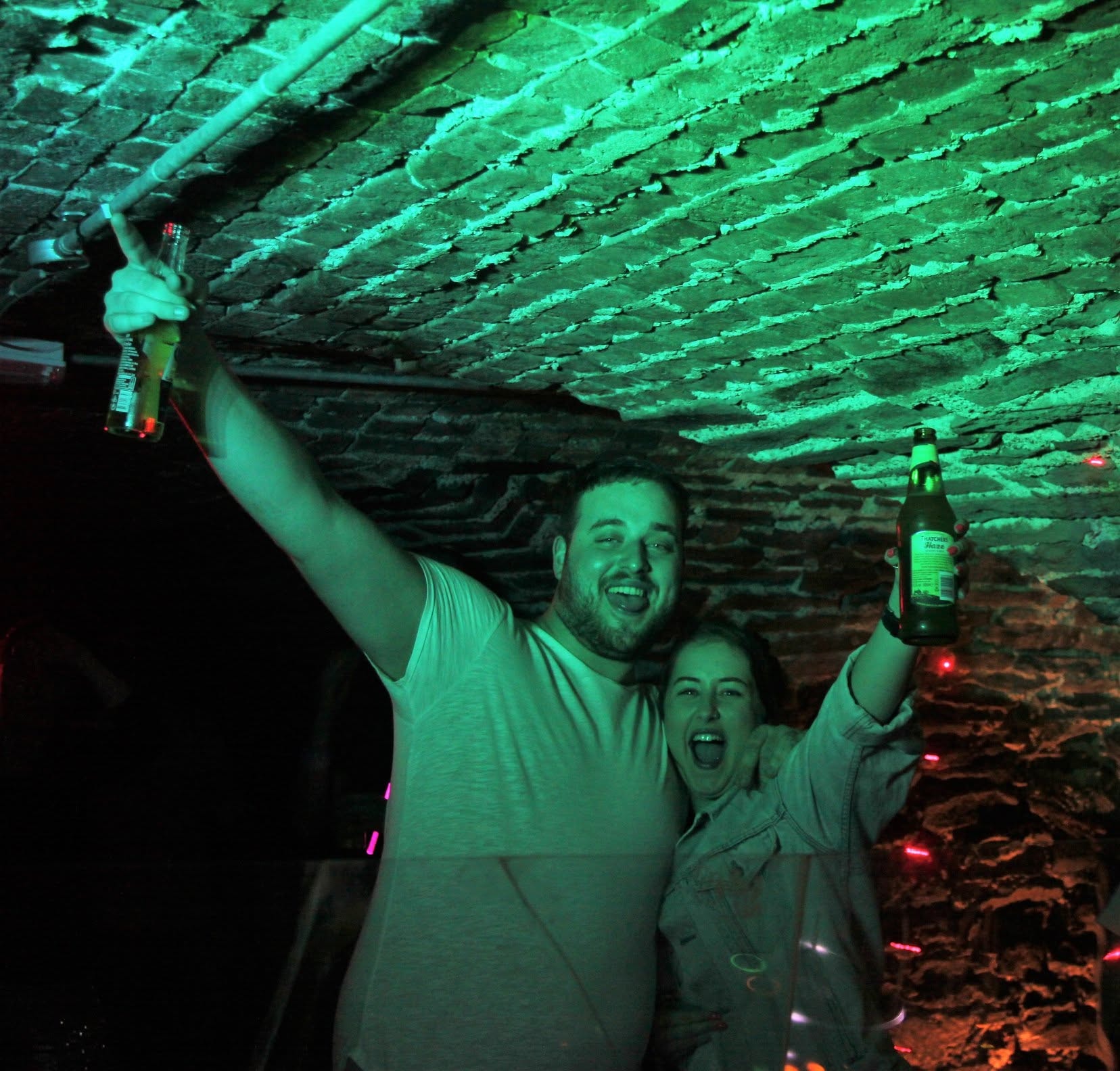 Revellers under green-lit brick ceiling